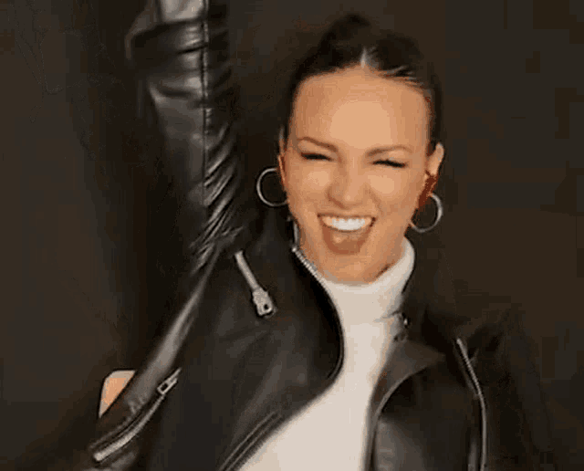 a woman in a black leather jacket is holding a glass of blue liquid in her hand .