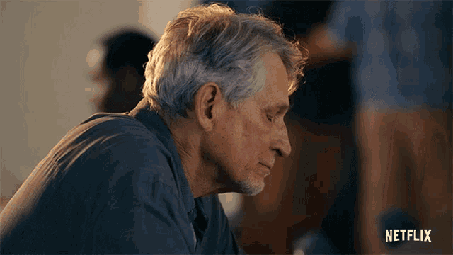 a man with gray hair and a beard sits in front of a sign that says netflix