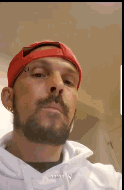 a man with a beard wearing a red hat and a white hoodie has a time stamp of 00:00:04