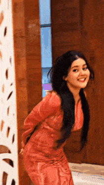 a woman in a pink dress is standing in front of a wooden door and smiling .
