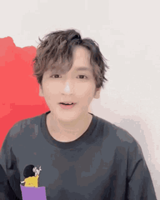 a young man wearing a black t-shirt with a cartoon character on it is standing in front of a red wall .