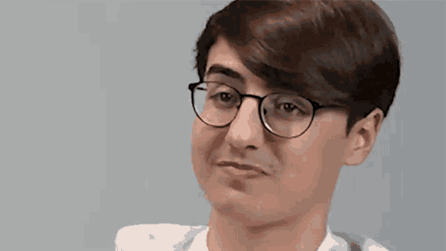 a young man wearing glasses and a white shirt is making a silly face .