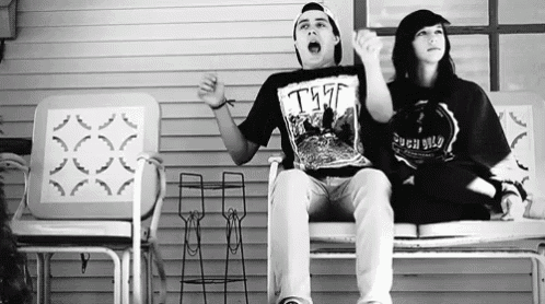 a man and a woman are sitting on a porch and the man is wearing a tshirt that says t77
