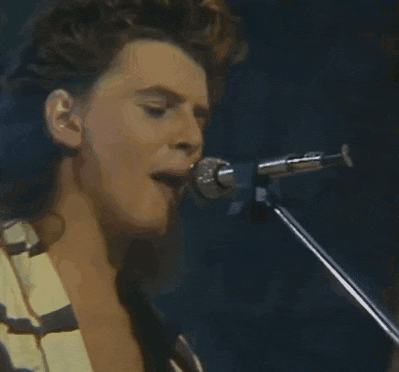 a man singing into a microphone with a guitar in the background