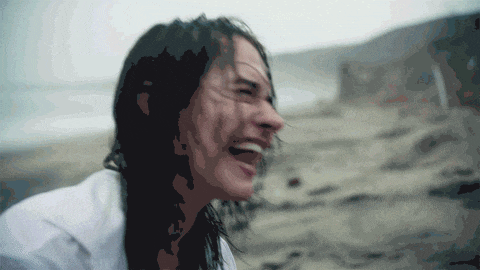 a woman with long hair is laughing on the beach