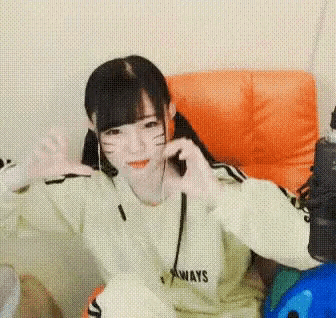 a girl is making a heart shape with her hands while sitting in an orange chair .