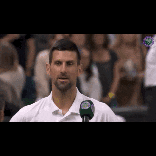 a man in a white shirt is talking into a microphone with a wimbledon logo in the background