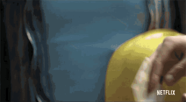 a close up of a person holding a yellow balloon with a netflix logo in the corner