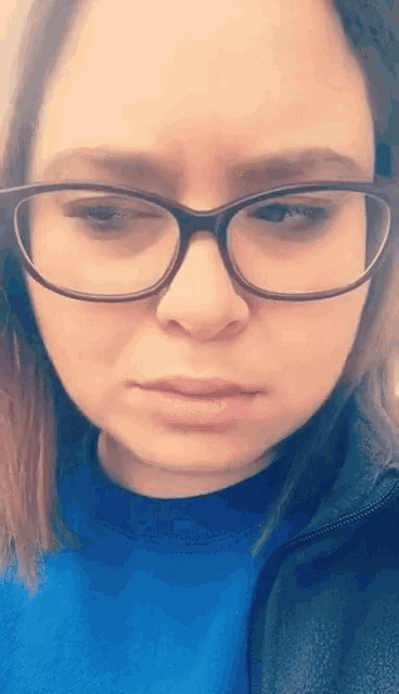 a woman wearing glasses and a blue shirt looks serious