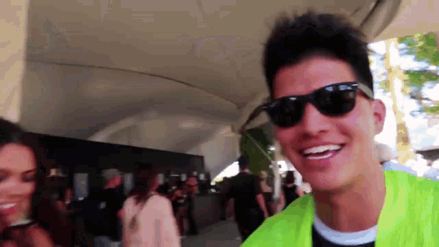 a man wearing sunglasses and a neon green jacket smiles in front of a crowd