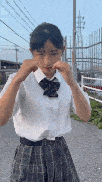 a girl in a white shirt and plaid skirt is standing in front of a fence .
