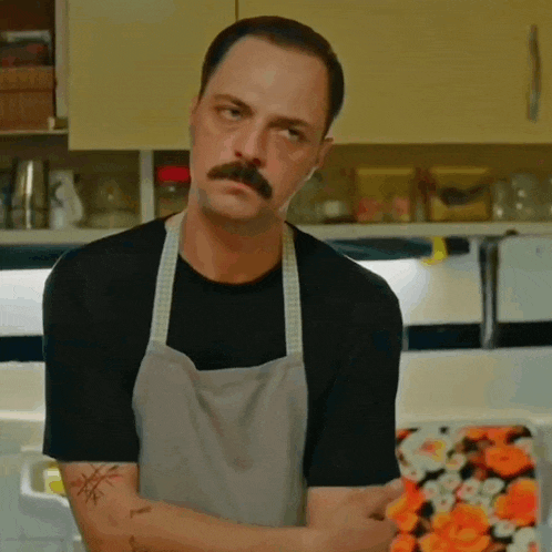 a man with a mustache is wearing an apron and has a tattoo on his arm