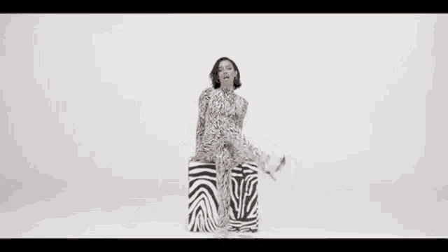 a woman in a zebra print jumpsuit is sitting on a box .