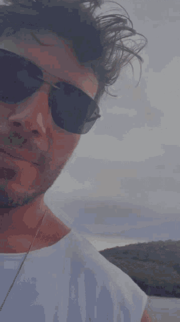 a man wearing sunglasses and a white shirt is looking at the camera