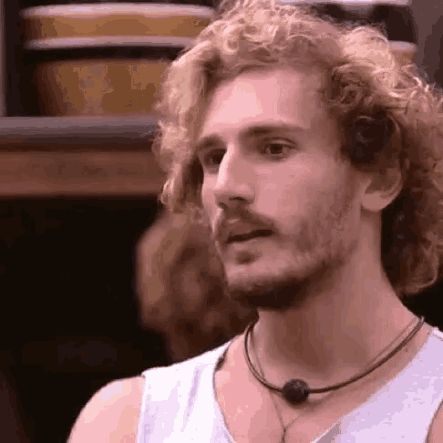 a man with curly blonde hair and a beard is wearing a necklace .