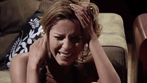 a woman is crying while sitting on a couch holding her head .