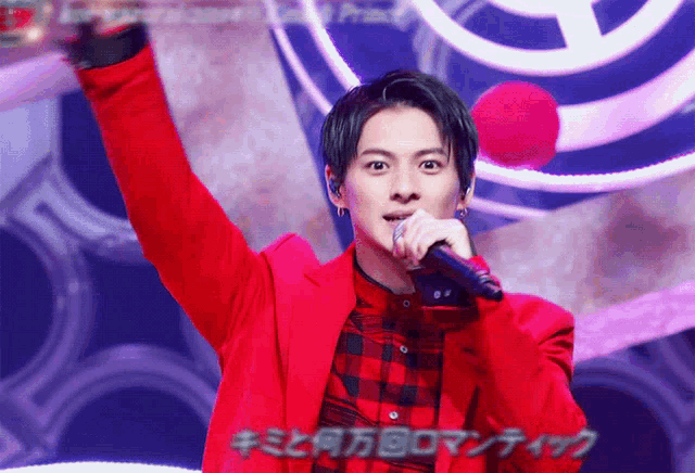 a man in a red jacket is singing into a microphone with foreign writing behind him