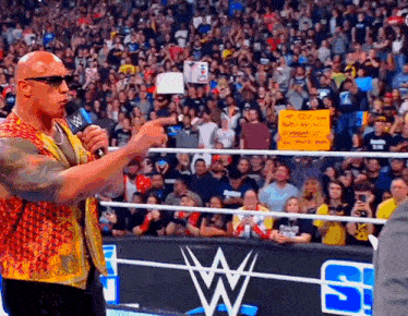 a wrestler is speaking into a microphone in front of a crowd at a wrestling match