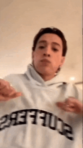 a man is wearing a white hoodie and making a face .