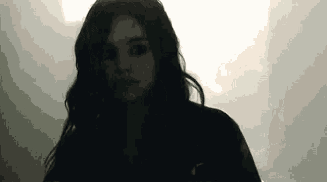 a woman with long black hair is standing in a dark room .