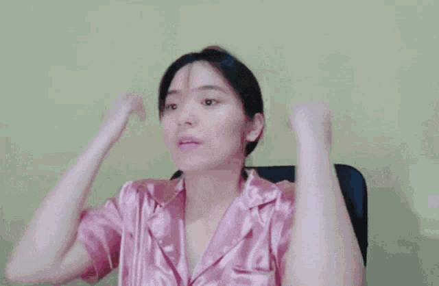 a woman wearing a pink satin pajama top is sitting in a chair