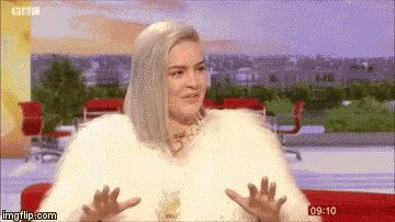 a woman is sitting on a couch wearing a fur coat and making a funny face .