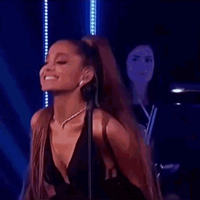 ariana grande is smiling and dancing on stage while holding a microphone .