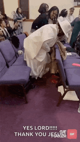 a group of people are sitting in purple chairs in a church and a woman is kneeling on the floor .