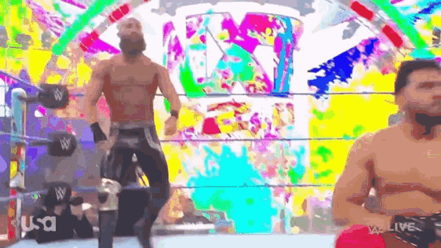 a man with a beard is standing in a wrestling ring in front of a colorful background .