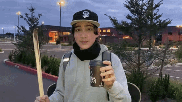 a young man holding a skateboard and a cup of coffee with a s on it