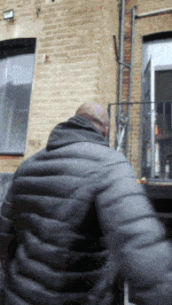 a man in a black jacket is standing in front of a brick wall