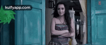 a woman in a strapless dress is standing in front of a door with her arms crossed .