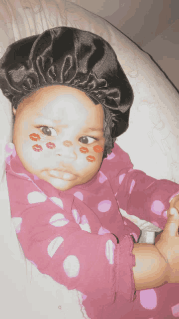 a baby wearing a hat and polka dot pajamas has red kisses drawn on her face