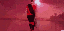 a man in a red shirt and black shorts is walking with a suitcase and a briefcase .