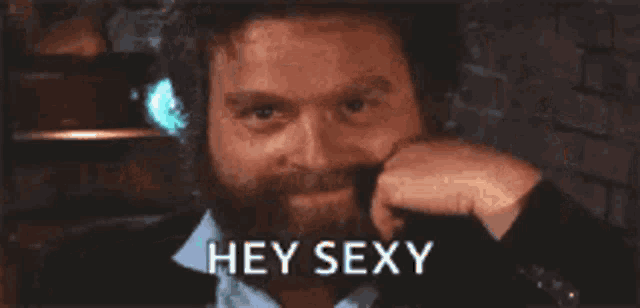 a man with a beard is holding his hand to his face and says hey sexy