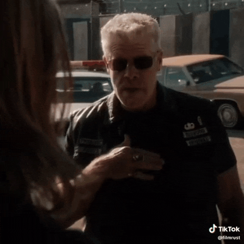 a man wearing sunglasses and a leather jacket is talking to a woman .