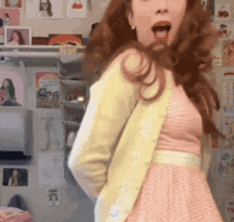 a woman wearing a pink dress and a yellow jacket is standing in a room .
