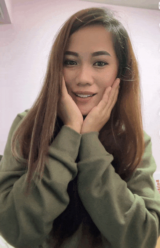 a woman wearing a green sweater is smiling with her hands on her face