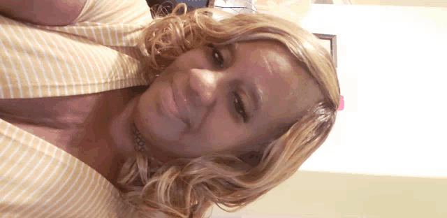 a woman with blonde hair and a yellow striped shirt smiles