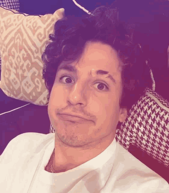 a man with curly hair is making a funny face in front of a patterned pillow