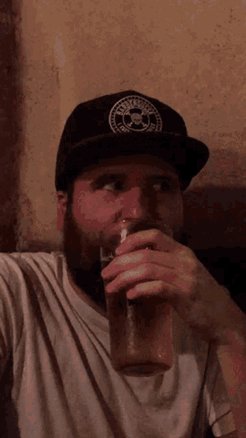 a man wearing a hat with a skull and crossbones logo drinking from a glass