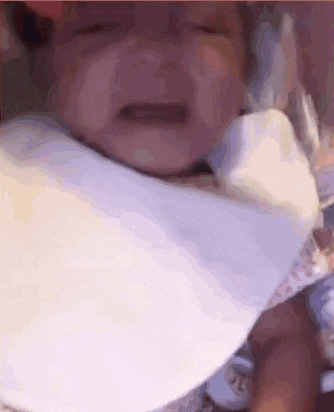 a baby is wearing a bib and crying while being held .