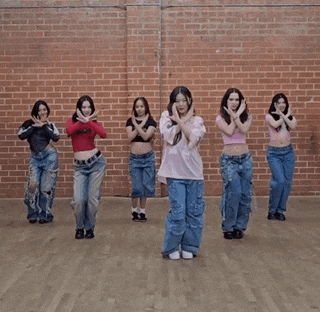 a group of young women are dancing in a room with a brick wall