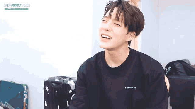 a young man wearing a black sweater is laughing while sitting in front of suitcases .