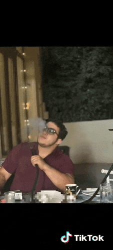 a man wearing sunglasses is smoking a hookah with tiktok written on the bottom of the screen