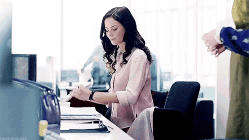 a woman is sitting at a desk writing on a clipboard .