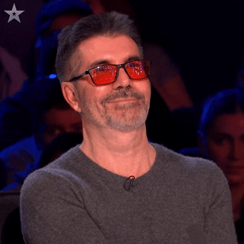 a man wearing red glasses and a grey sweater has a star on his chest