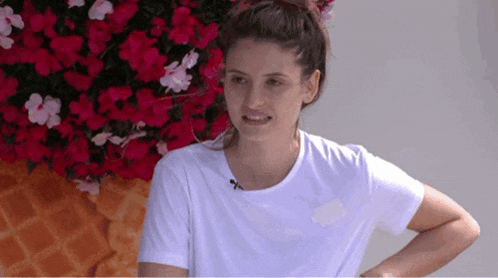 a woman in a white t-shirt is standing in front of an ice cream cone with pink flowers behind her .