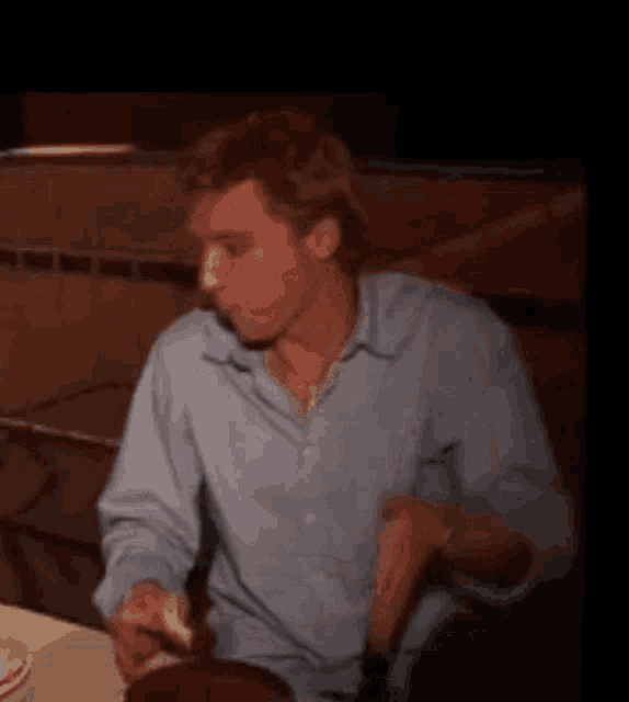 a man in a blue shirt is sitting at a table eating a piece of food