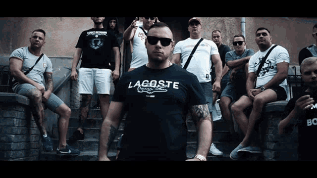 a man wearing a lacoste shirt stands in front of a group of people